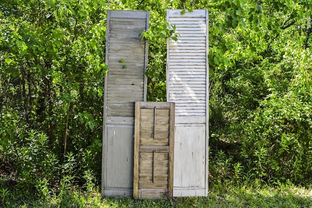 Three wooden shutters are stacked on top of each other in the grass.