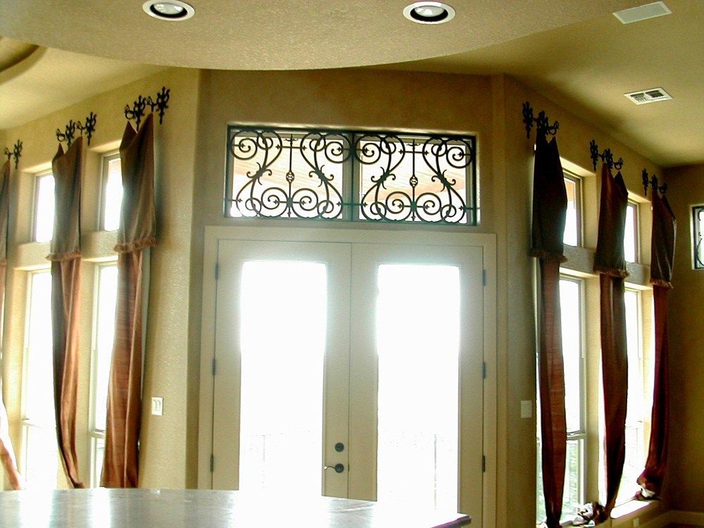 A corner of a room with a wrought iron window and curtains