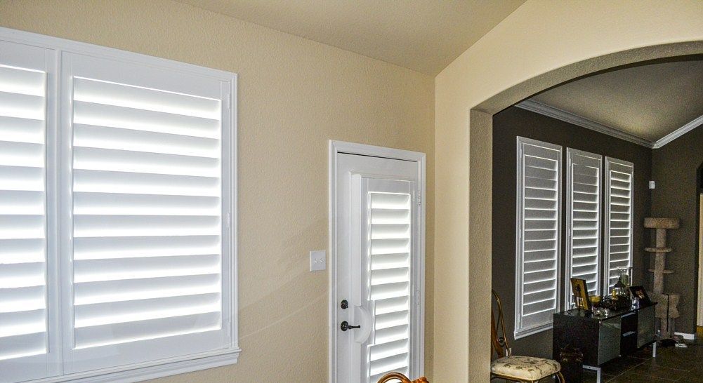 A living room with white shutters on the windows and a door.