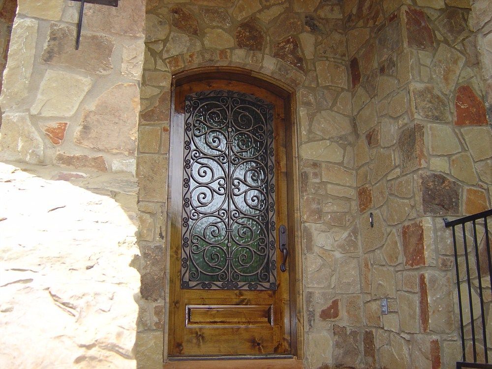 A wooden door with a wrought iron design is on a stone wall.