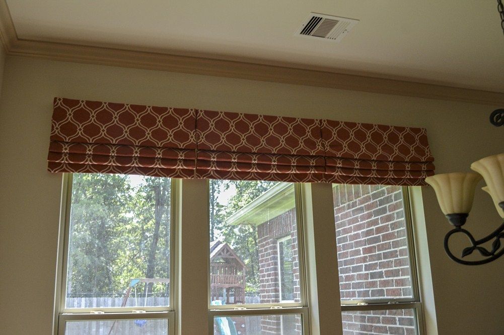 A window with a roman shade and a chandelier hanging from the ceiling