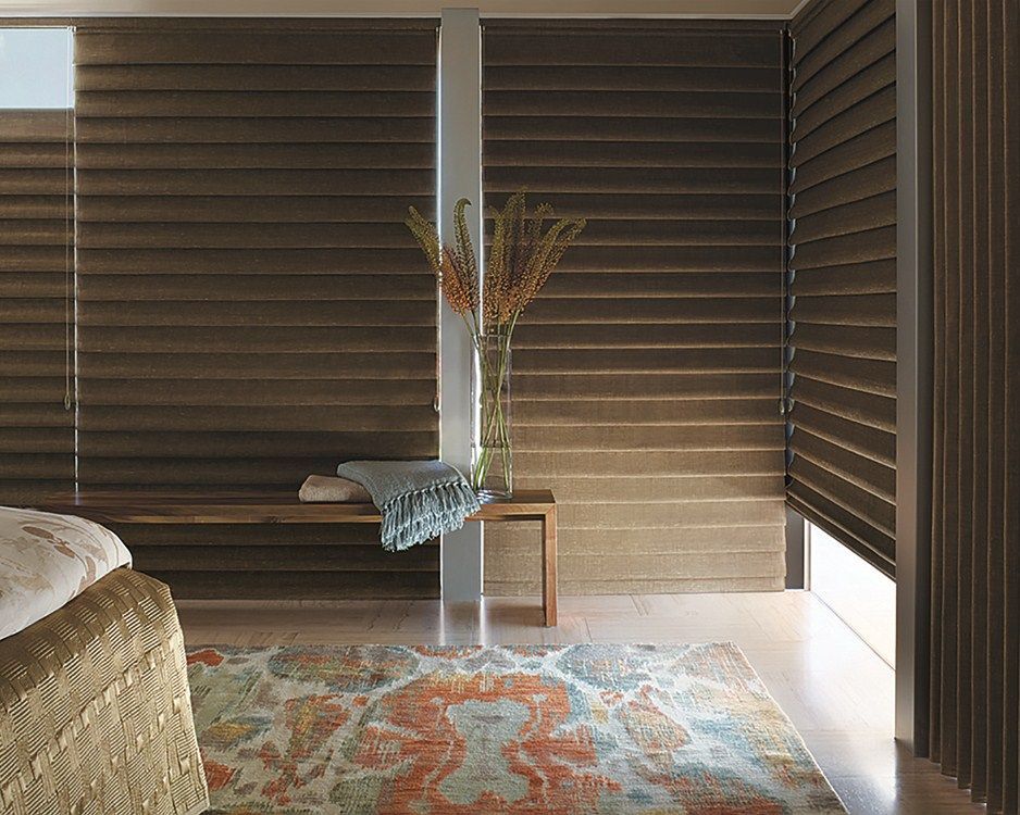 A bedroom with a bed , bench , rug and window shades.