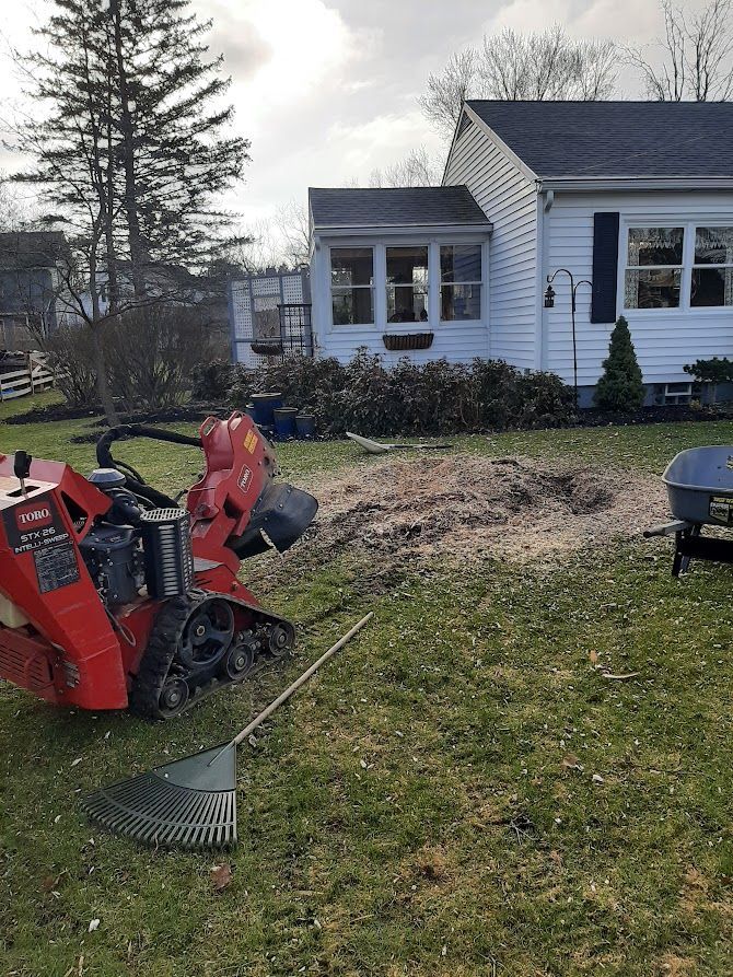 Red snow blower on a lawn beside a white house and a leaf rake in the foreground Red snow blower on a lawn beside a white house and a leaf rake in the foreground