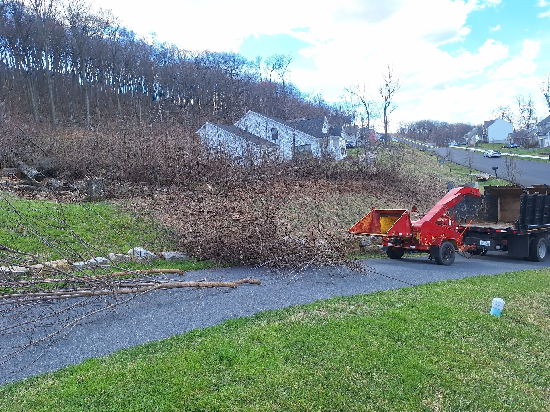 Red wood chipper beside a truck on a roadside slope with grass and bare trees