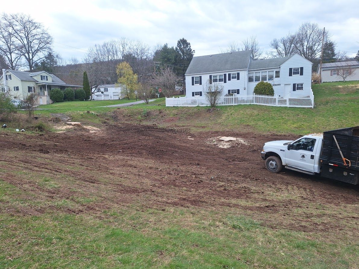 Dirt lot with a white truck at right, backed by suburban houses and leafless trees under a gray sky Dirt lot with a white truck at right, backed by suburban houses and leafless trees under a gray sky