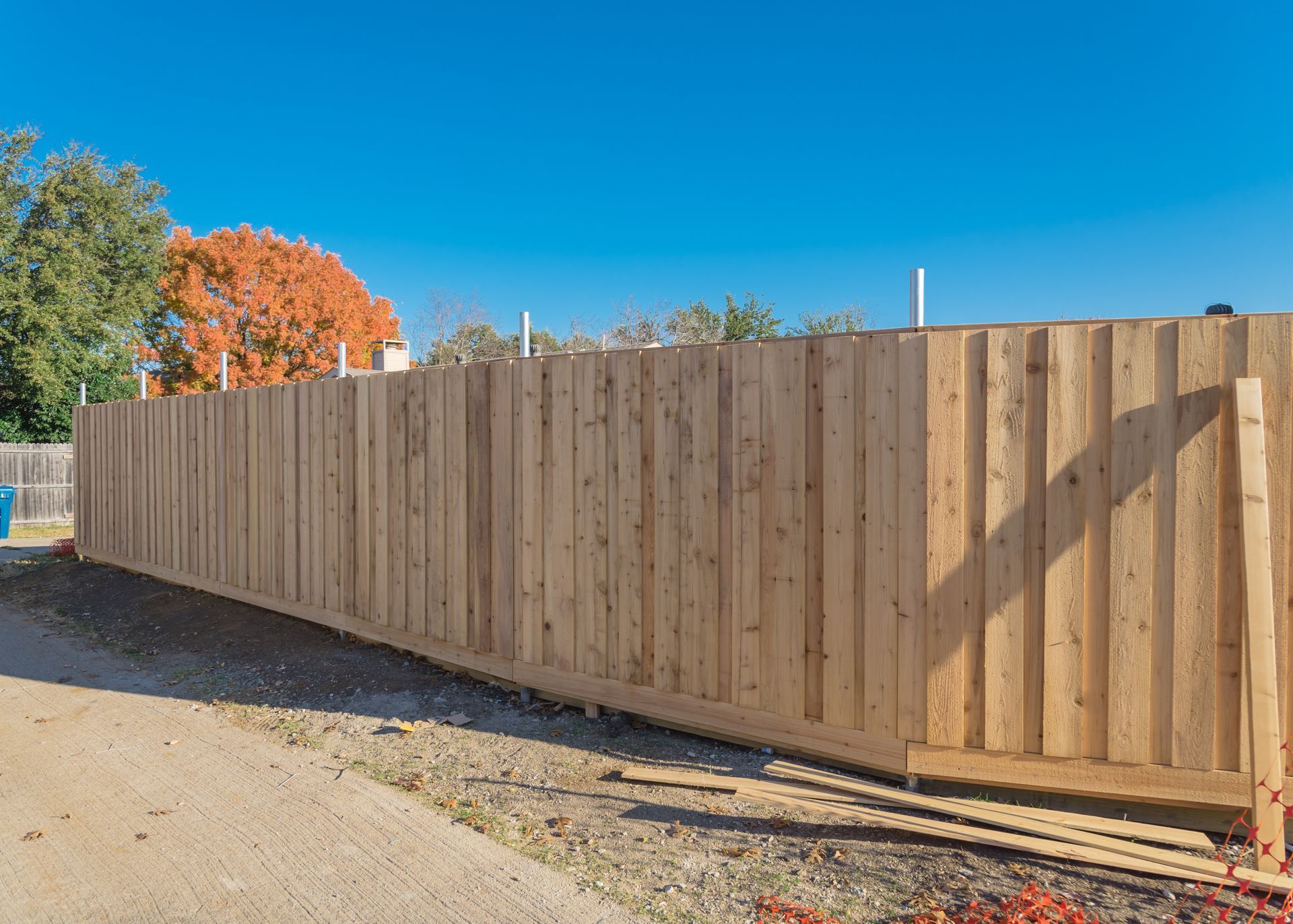 Wooden privacy fence along a gravel roadside under a clear blue sky