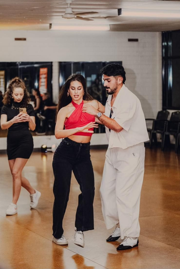 Two women are dancing on a wooden floor in front of a red curtain.
