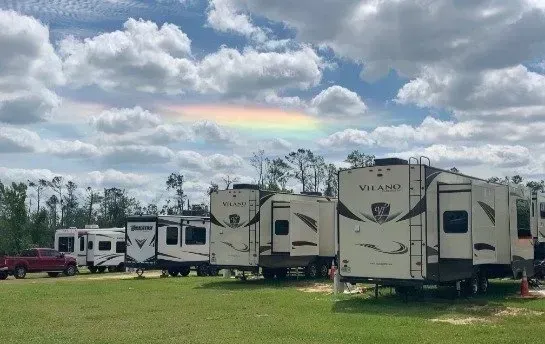 A row of rvs parked in a field with a rainbow in the sky.
