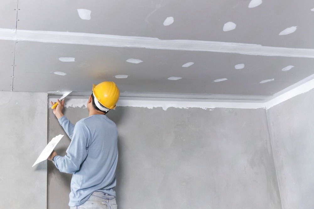 A man is plastering the ceiling of a room.