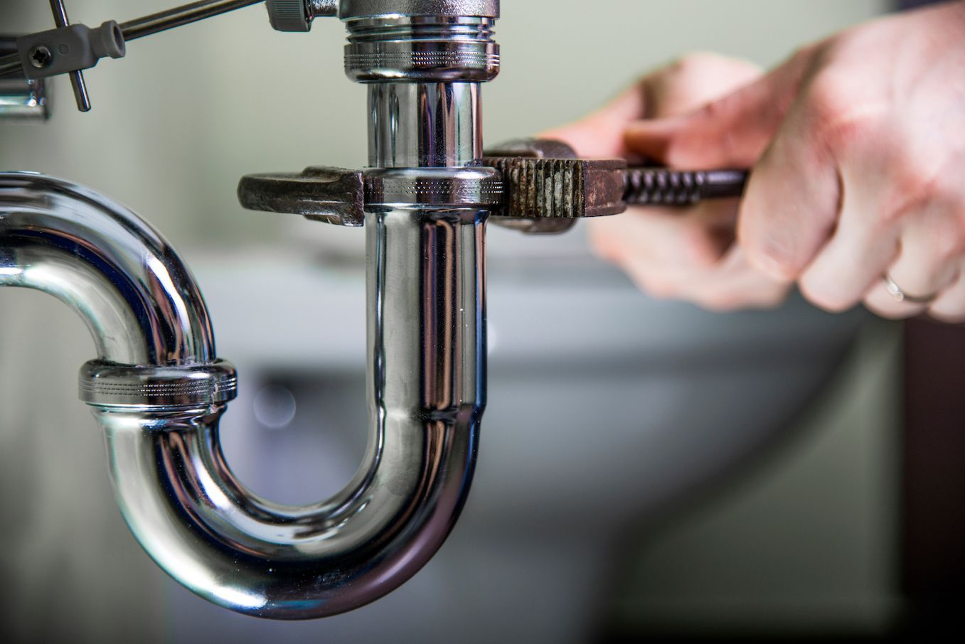 A plumber is fixing a sink pipe with a wrench.