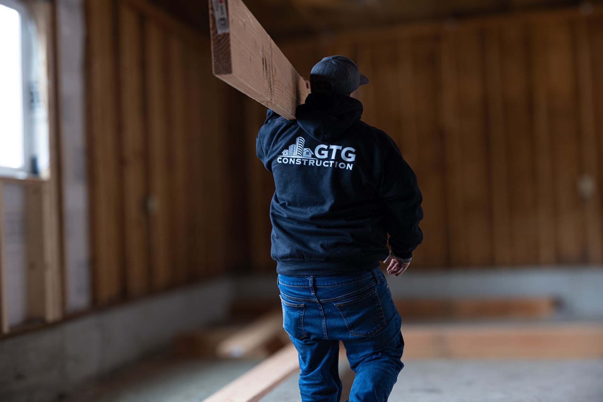 Construction worker carrying a beam on his shoulder and wearing a GTG Construction sweat shirt.