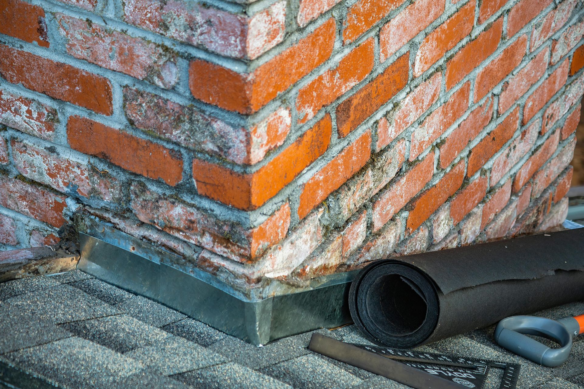 Close-up of a brick chimney corner with new flashing and rolled roofing material.