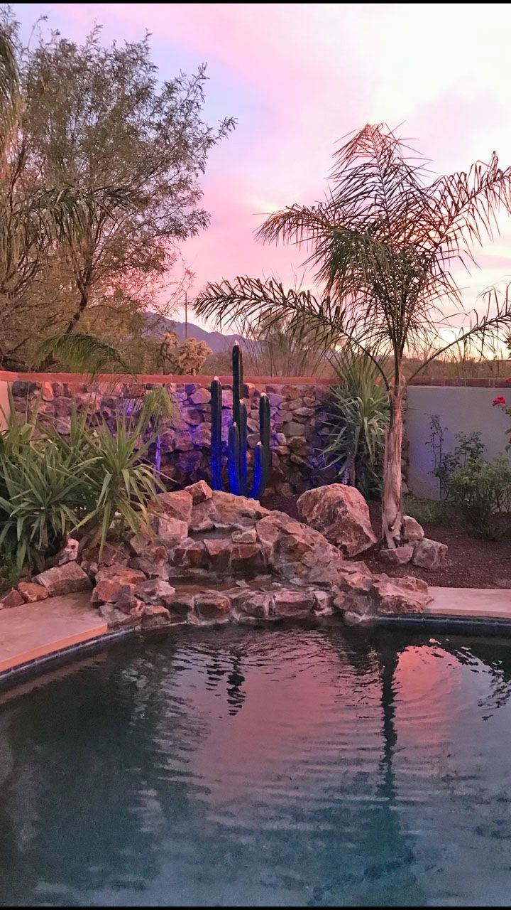 A swimming pool with a waterfall and a sunset in the background.