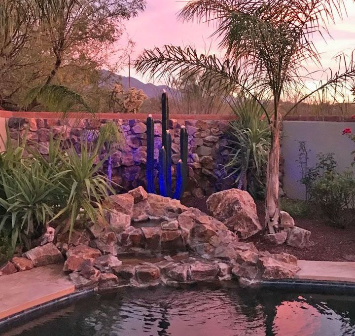 A swimming pool surrounded by rocks and palm trees at sunset