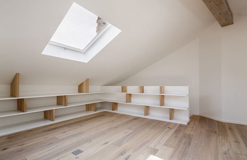 Luminosa mansarda con lucernario, pareti bianche, travi in legno e scaffalature a muro.