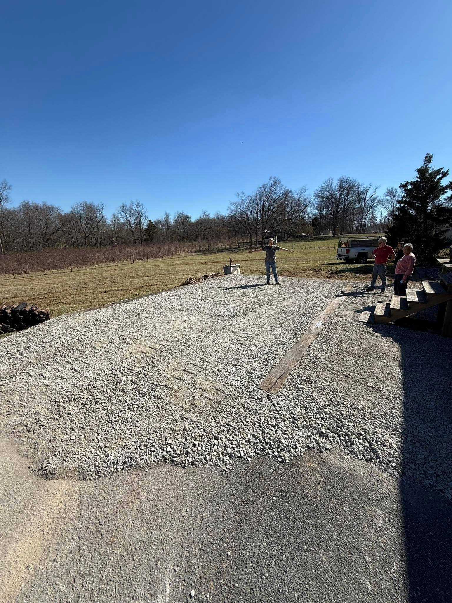 A group of people are standing on a gravel road in a field.