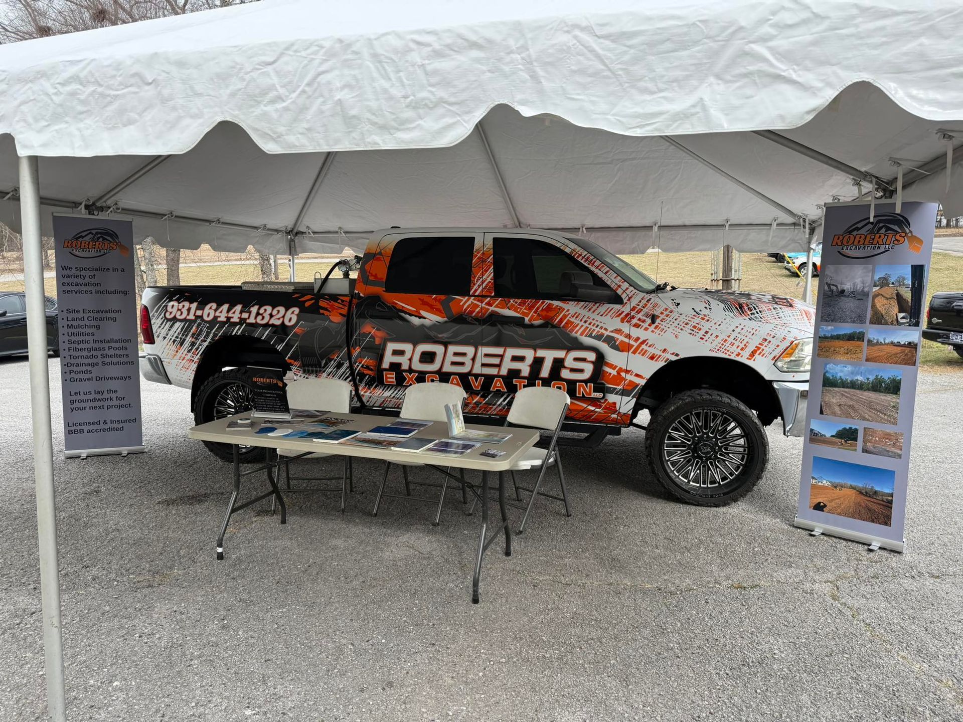 A truck is parked under a tent with a table and chairs.