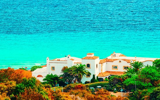 Edifici bianchi con tetti in terracotta, palme e oceano blu.