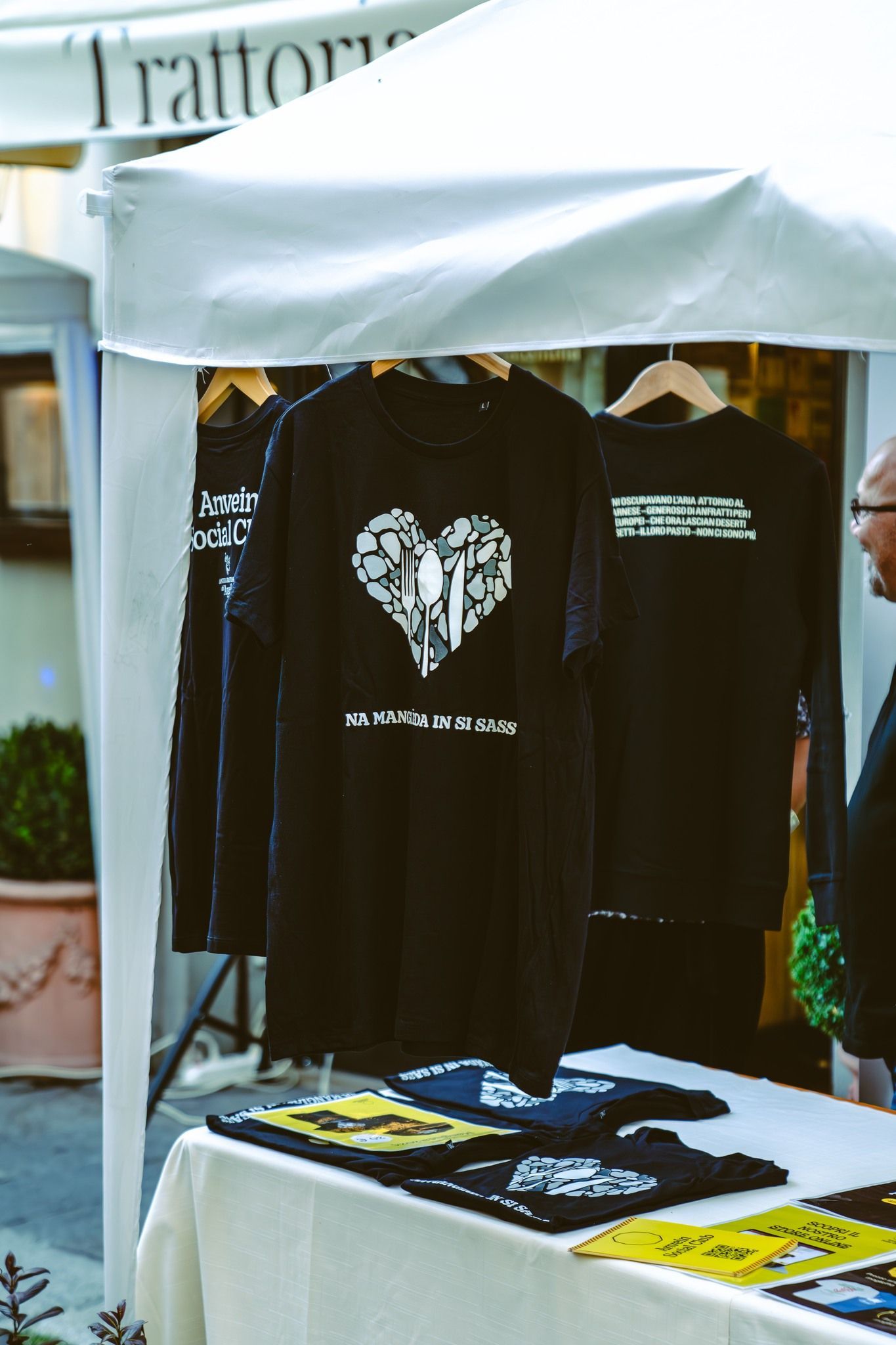 Magliette con disegni bianchi su sfondo nero esposte su una bancarella del mercato all'aperto.