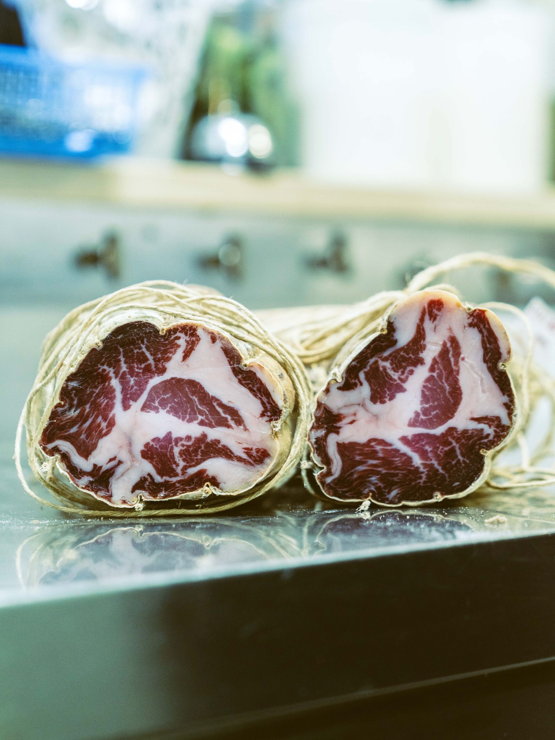 Carne stagionata, tagliata a fette per mostrare la polpa marmorizzata rossa e bianca, legata con spago, su una superficie di acciaio inossidabile.