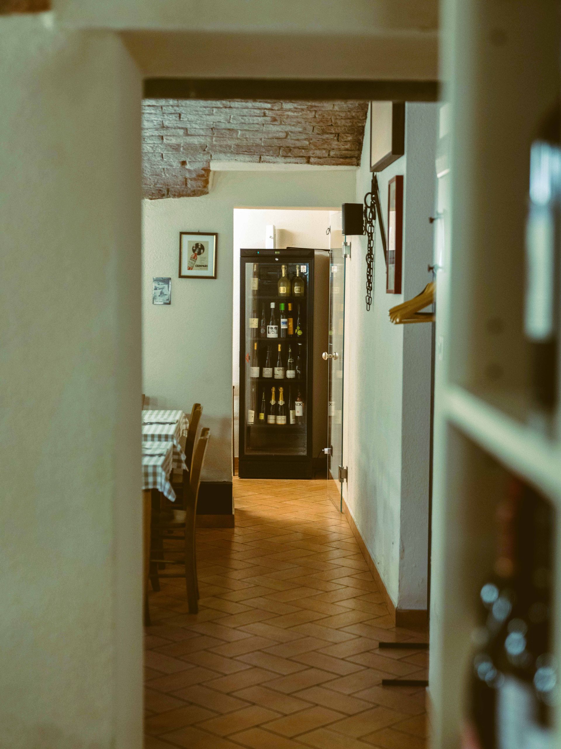 Corridoio stretto nel ristorante con pavimento in cotto, cantinetta per il vino e tavoli.