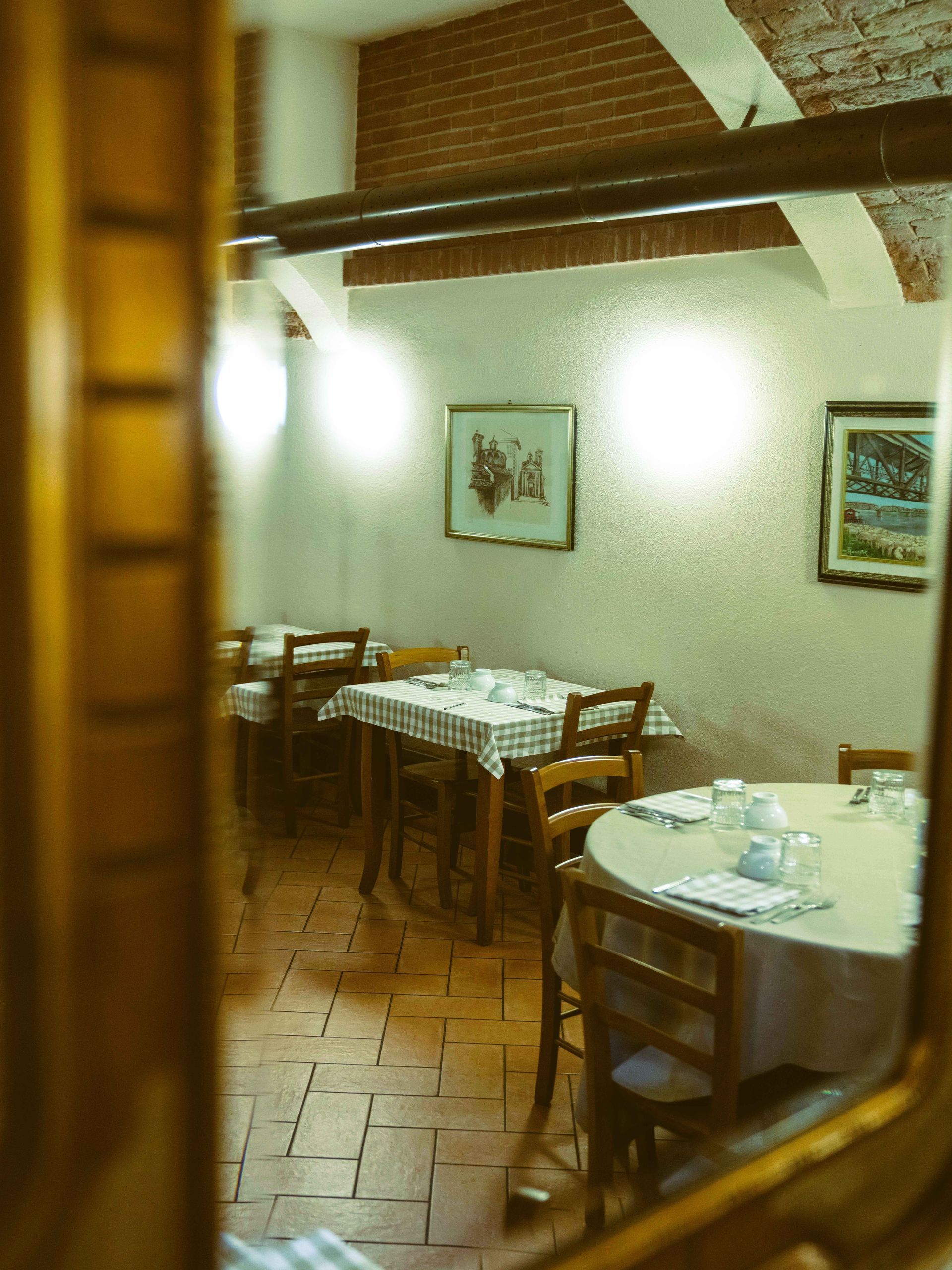 Sala da pranzo del ristorante con tavoli apparecchiati per il servizio, visibili attraverso un riflesso a specchio.