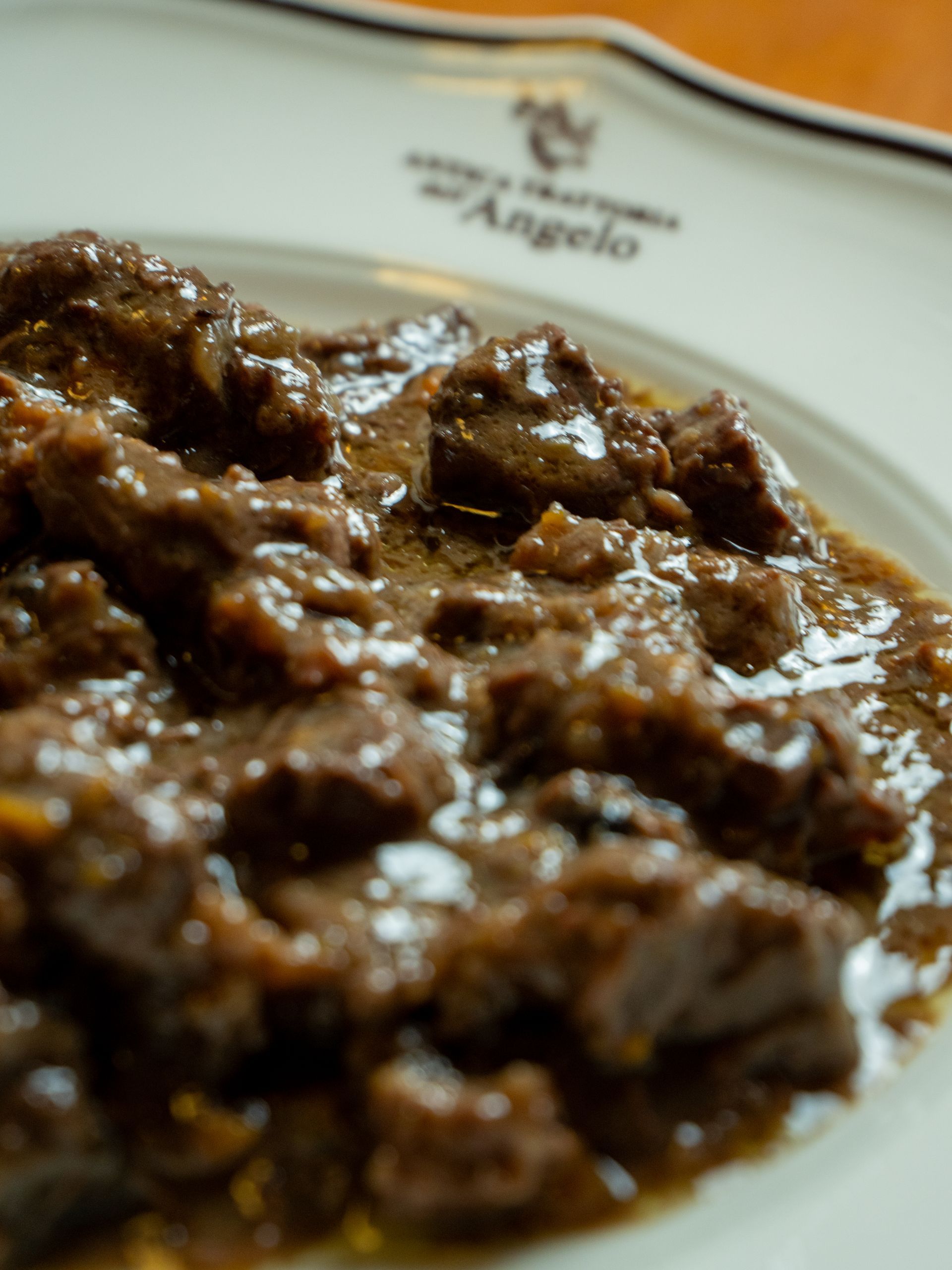 Spezzatino di manzo in salsa marrone servito su un piatto bianco; logo del ristorante visibile.