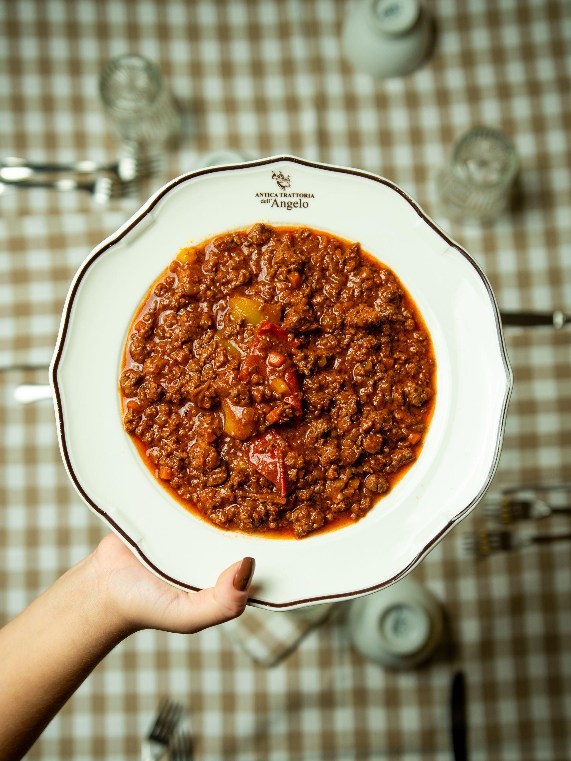 Persona che tiene in mano un piatto bianco ondulato, pieno di un ricco chili marrone.