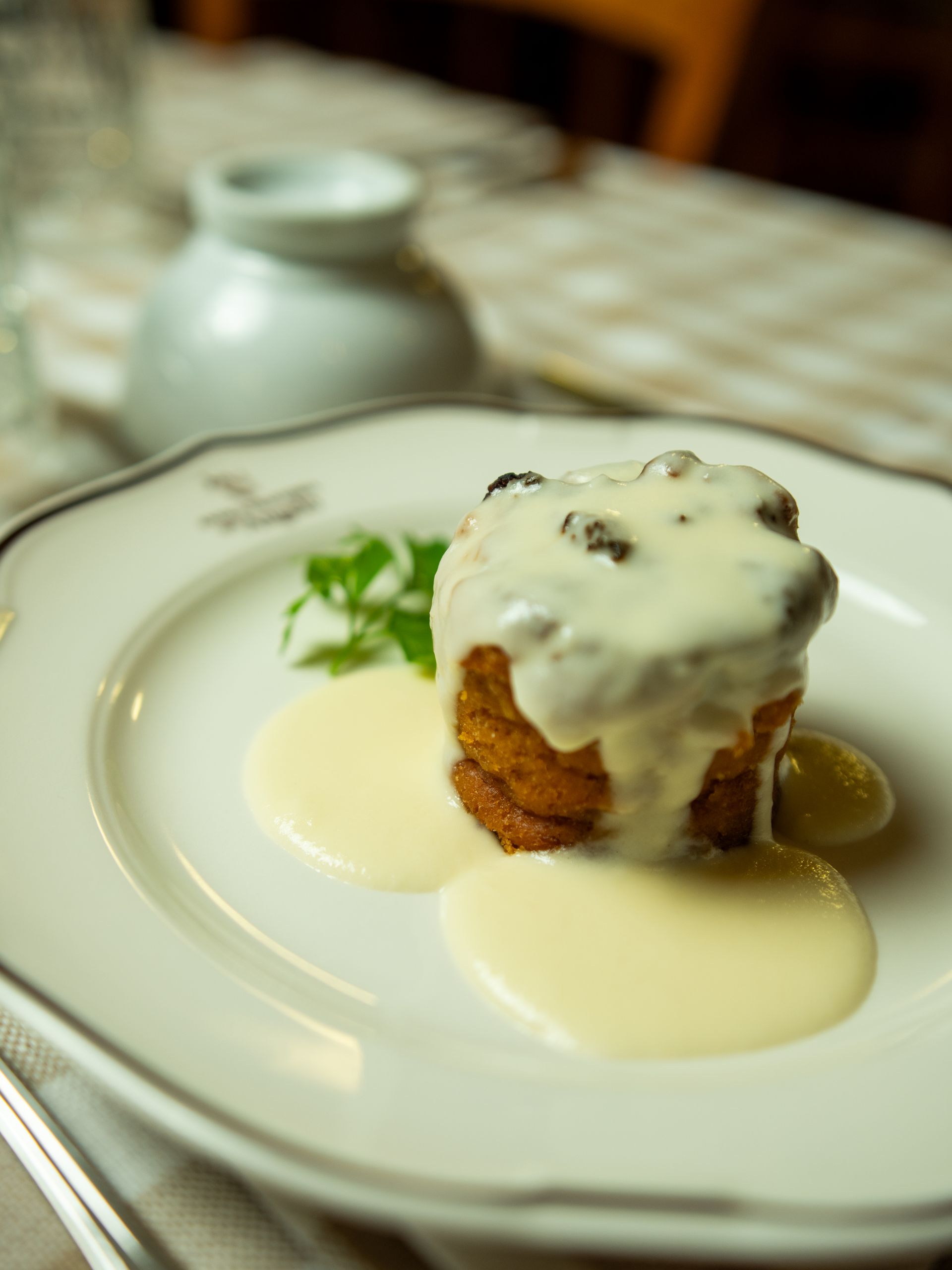 Una piccola torta con salsa bianca su un piatto bianco, con sullo sfondo una tavola apparecchiata.