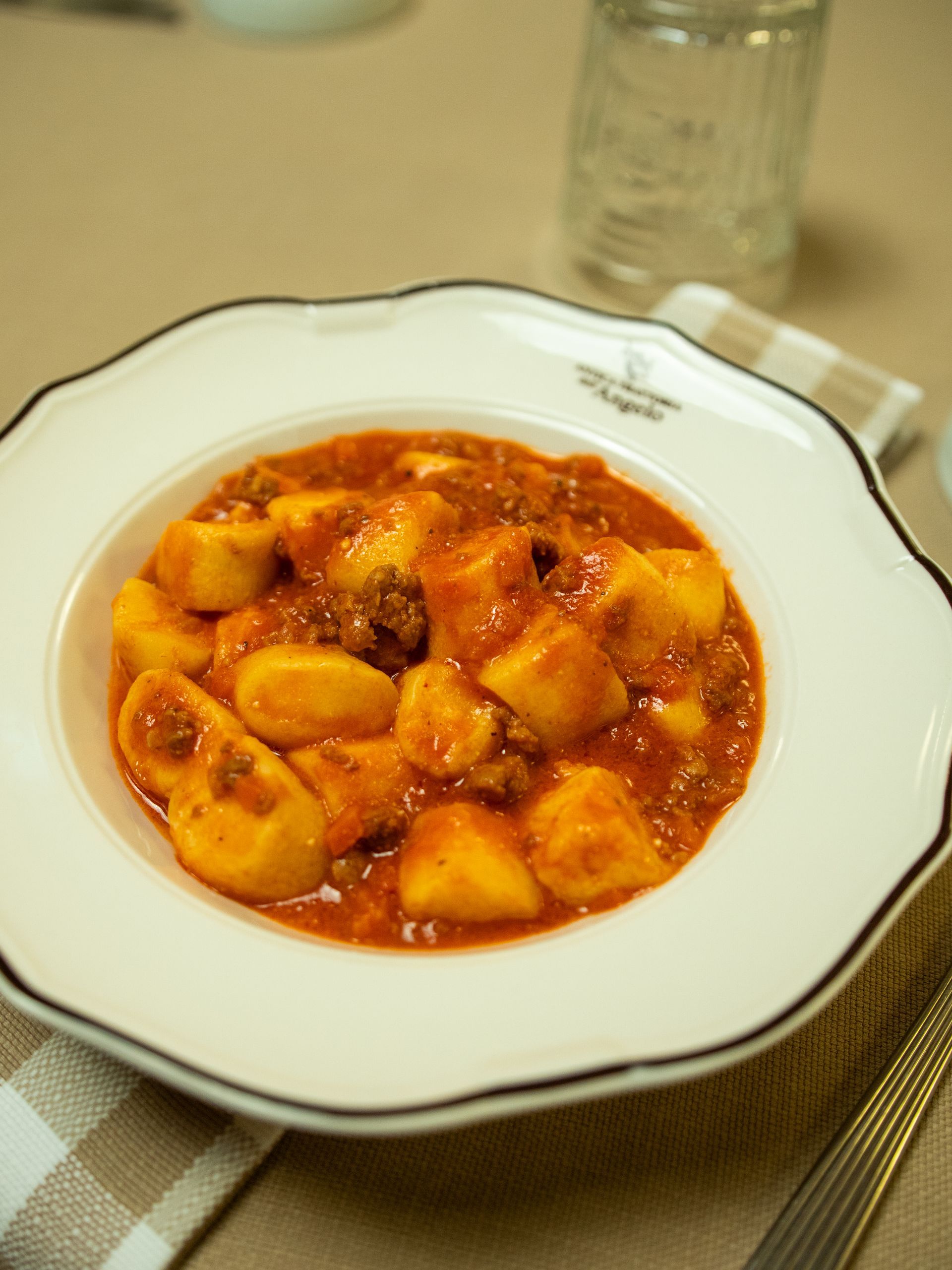 Gnocchi in salsa rossa in una ciotola bianca con i bordi smerlati, su un tovagliolo a quadretti.