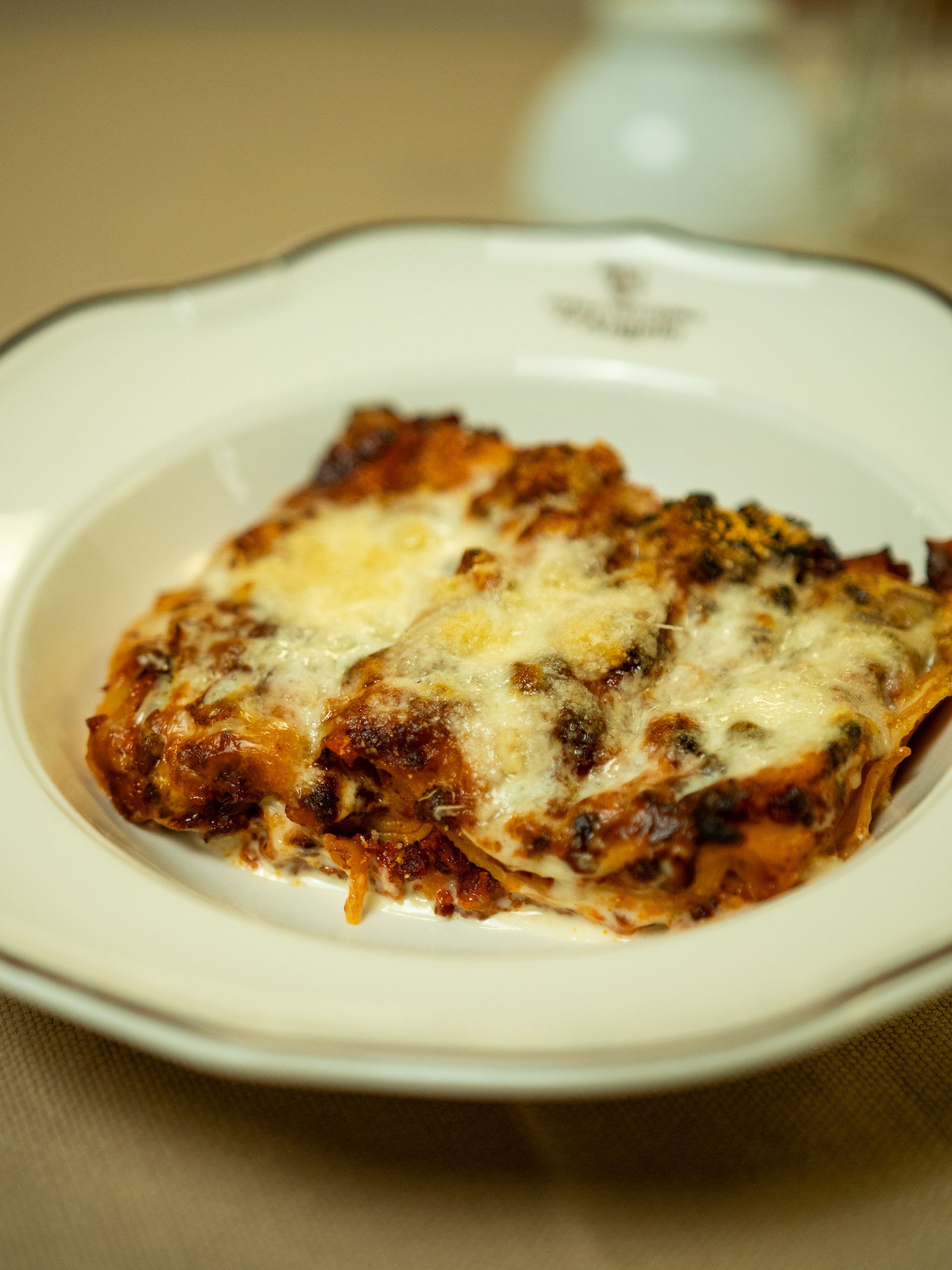 Lasagna su un piatto bianco con bordo marrone, guarnita con formaggio fuso.