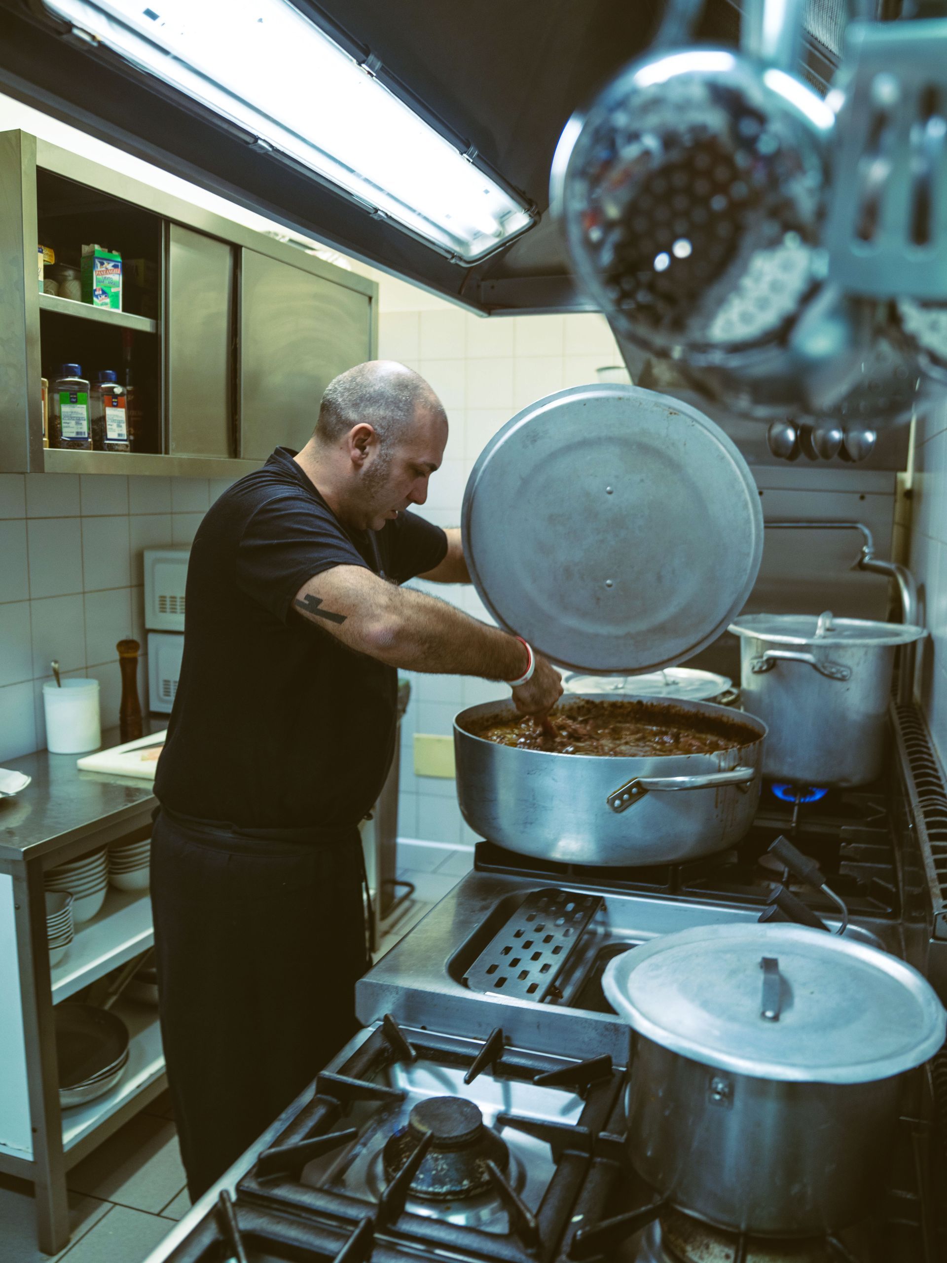 Uno chef mescola il contenuto di una pentola grande sul fornello di una cucina commerciale.