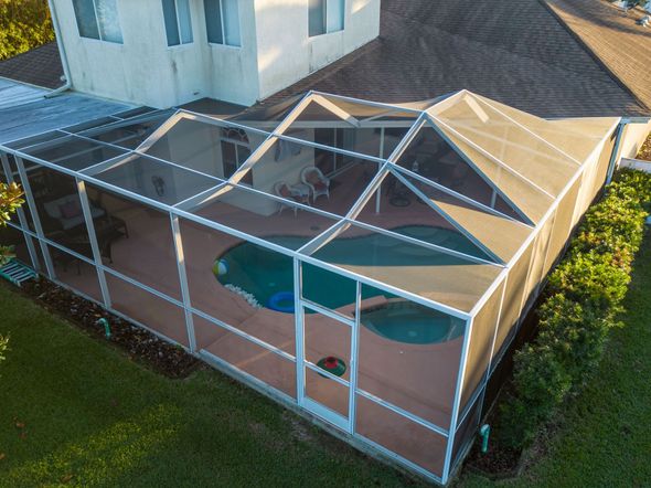 An aerial view of a screened in pool area with a house in the background.