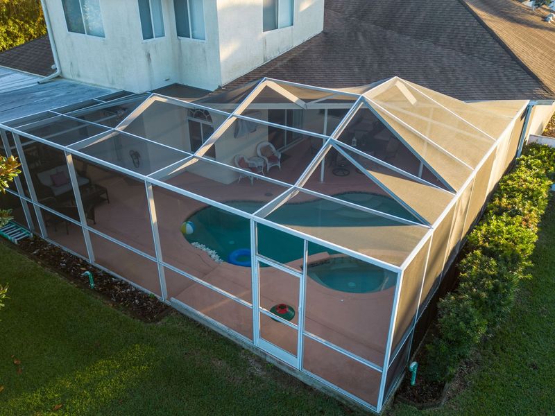 An aerial view of a screened in pool area with a house in the background.