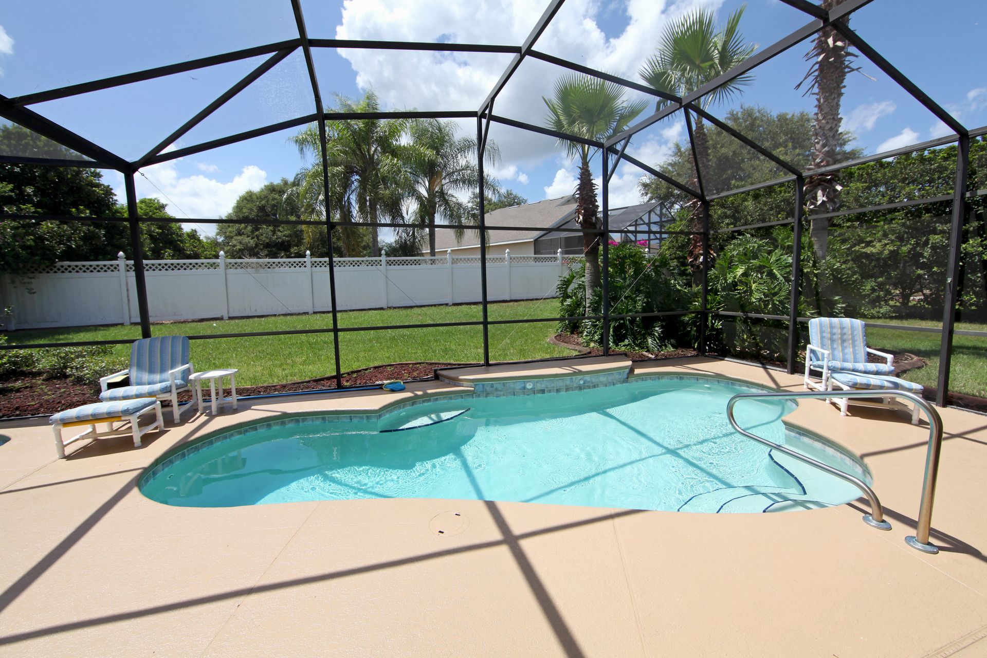 A screened in swimming pool with chairs and a fence in the background