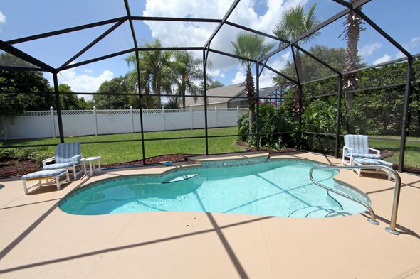 A screened in swimming pool with chairs and a fence in the background