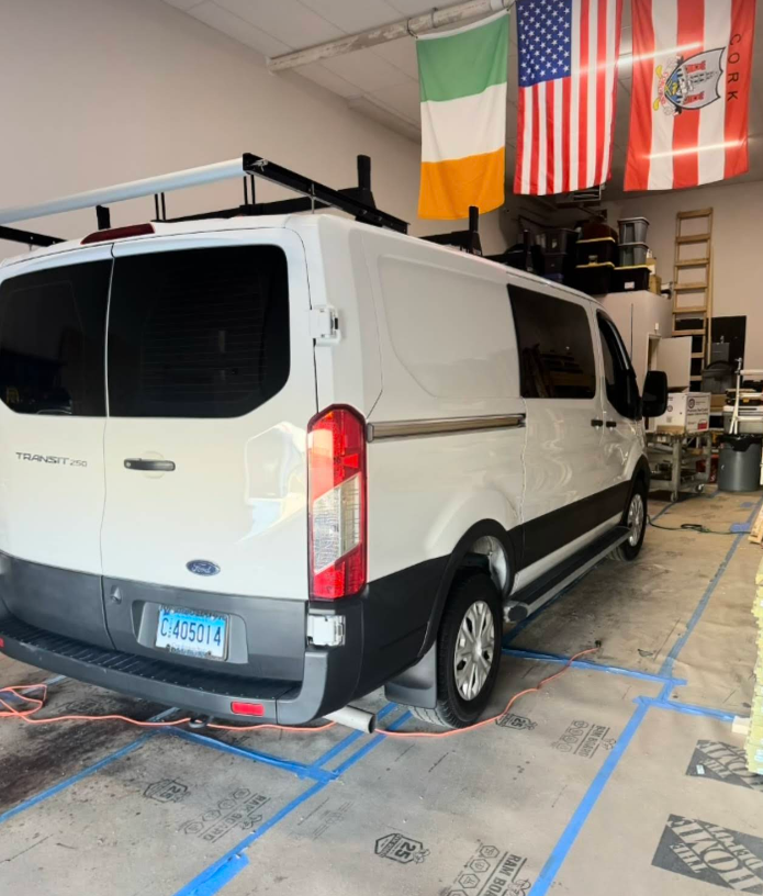 A white van is parked in a garage with flags hanging from the ceiling