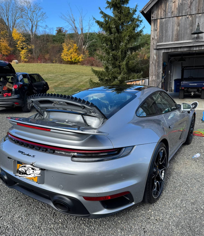 A silver porsche turbo is parked in front of a garage.