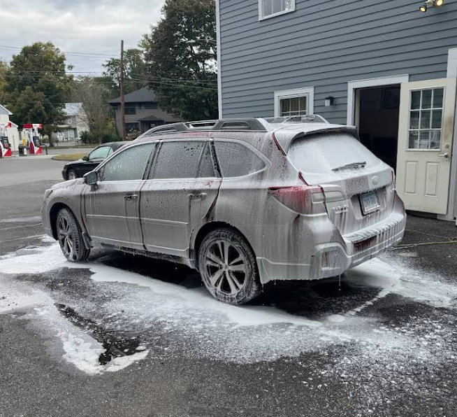 A silver suv is covered in foam in a parking lot.