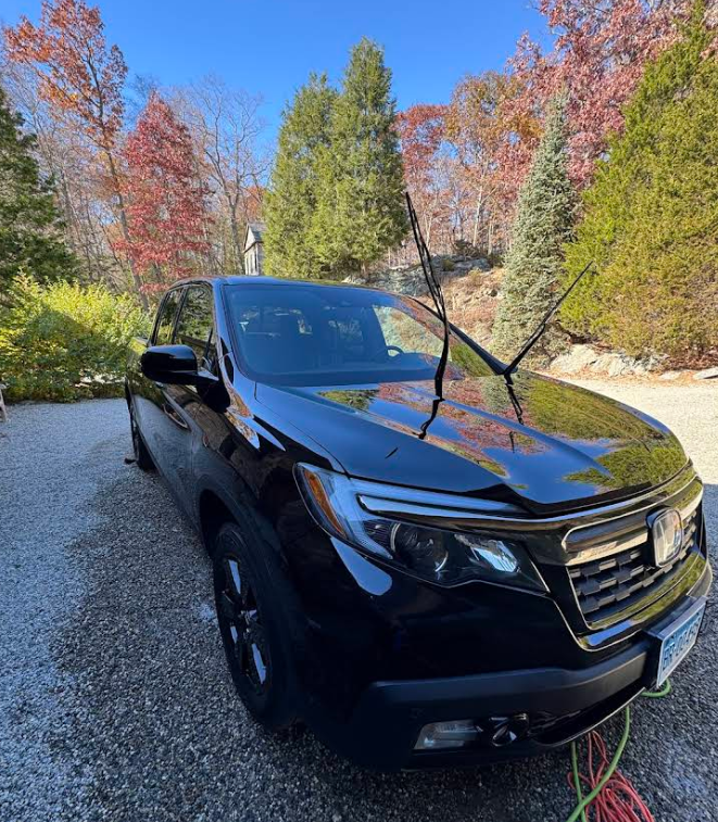 A black honda ridgeline is parked in a gravel driveway.