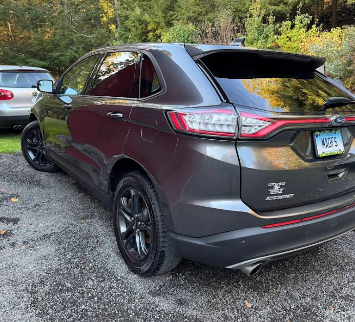 A gray ford edge is parked in a gravel lot
