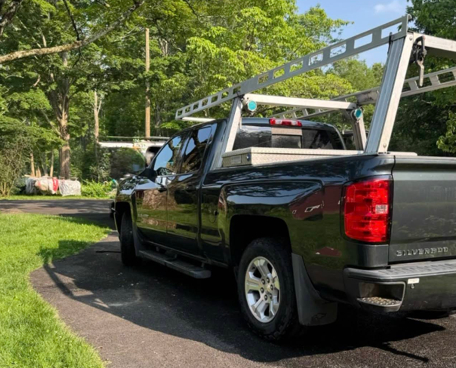 A black truck with a ladder rack on the back is parked on the side of the road.