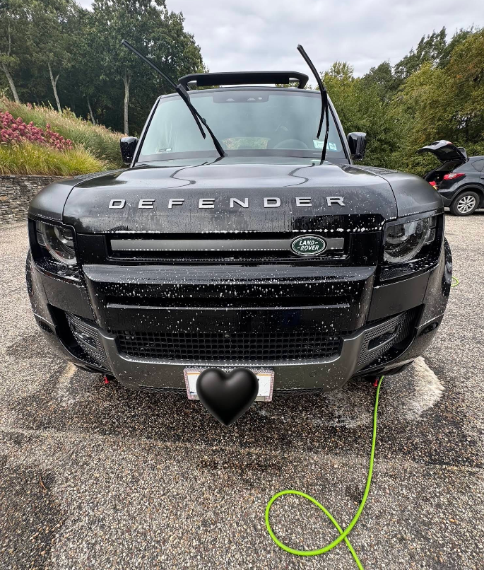 A black land rover defender is charging in a parking lot.
