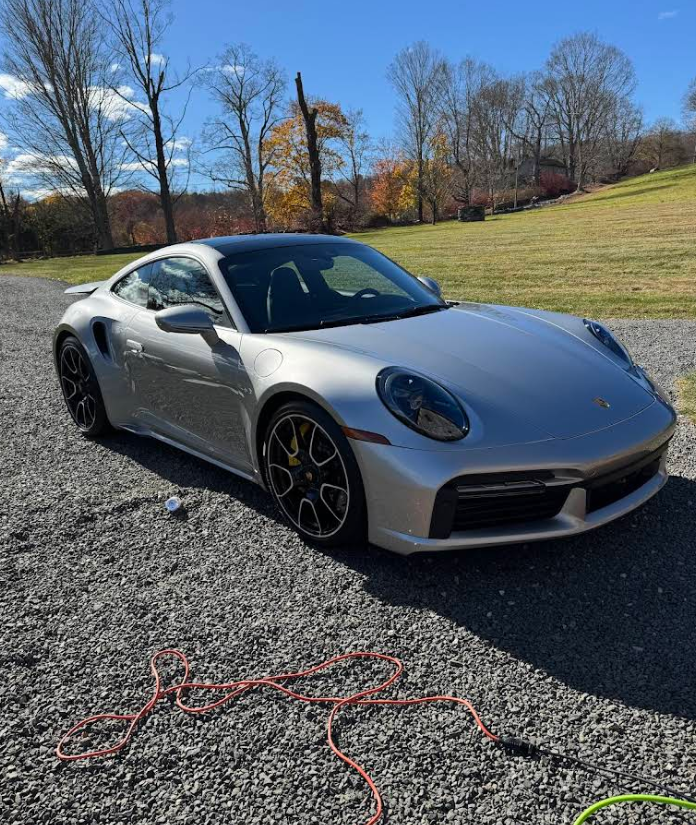 A silver porsche 911 turbo s is parked on a gravel road.