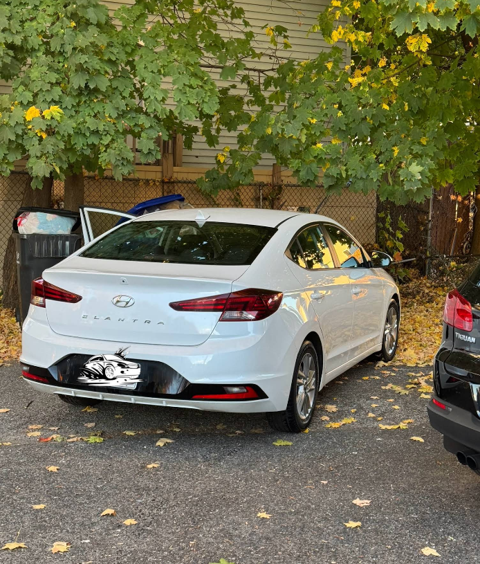 A white car is parked in a driveway next to a black car.