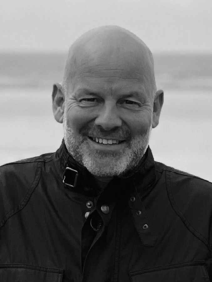 A bald man with a beard is smiling in a black and white photo.