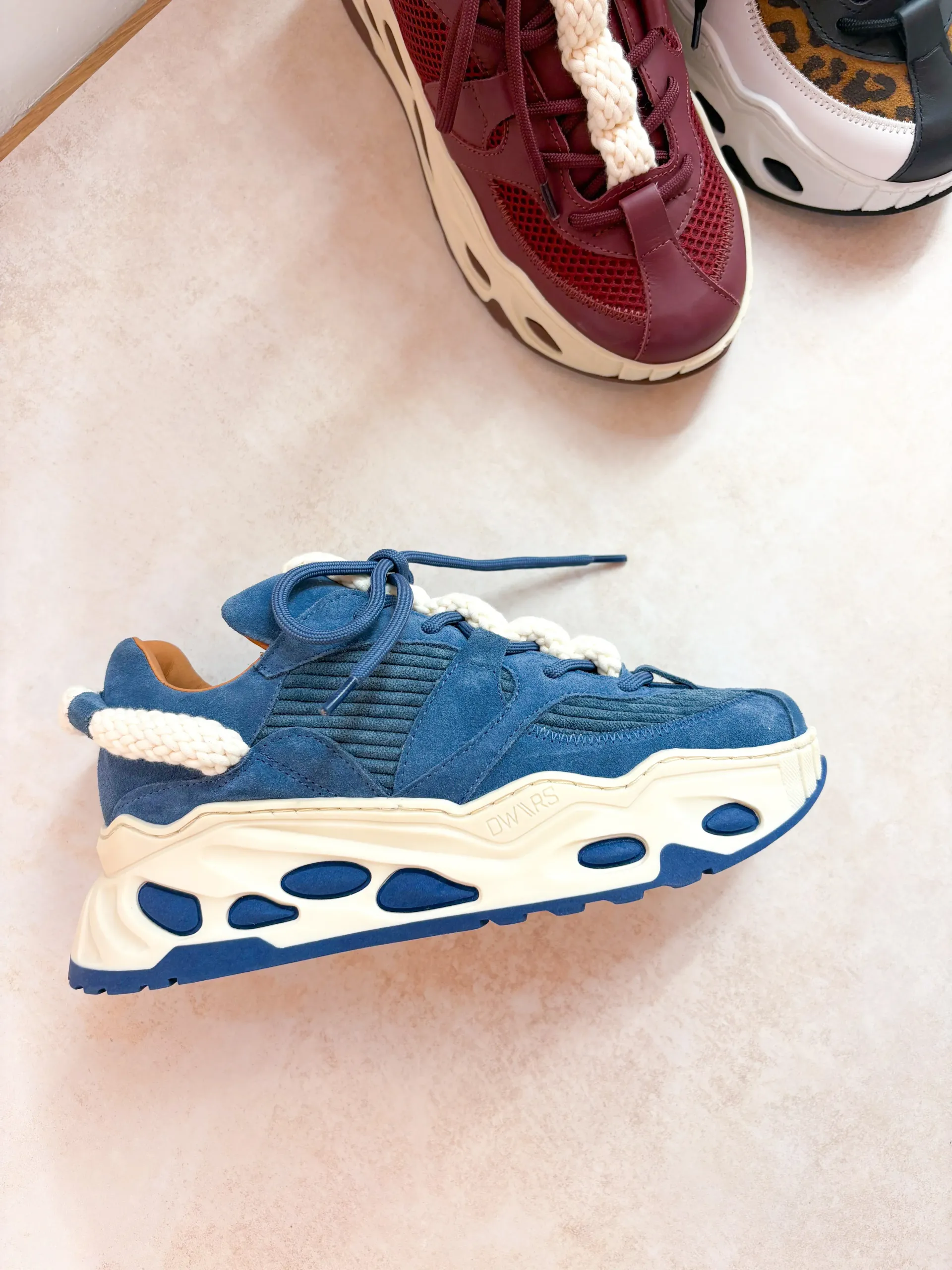 Blauwe en crèmekleurige sneaker met een dikke, golvende zool en stevige veters.