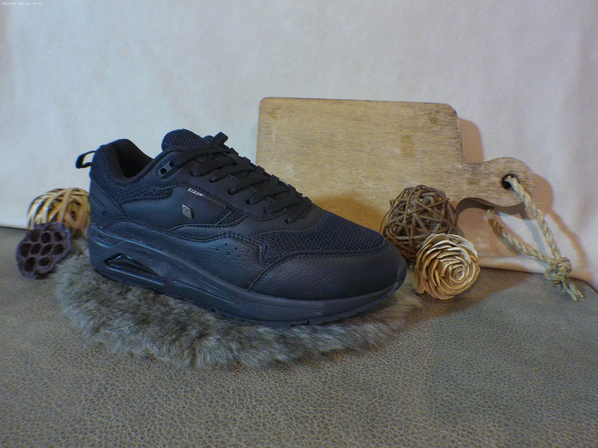Een paar zwarte sneakers liggen op een tapijt naast een houten snijplank.