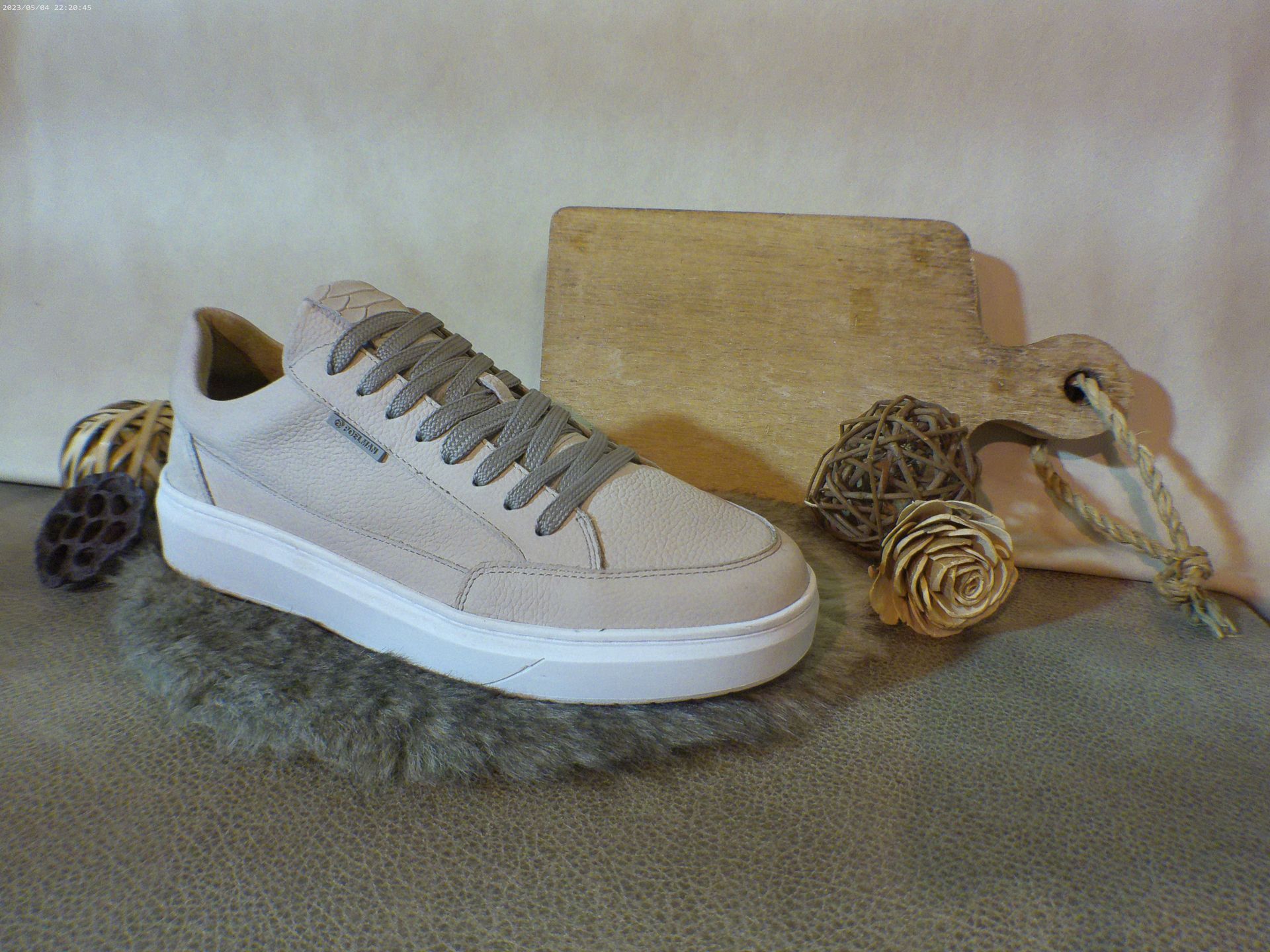 Een paar witte sneakers liggen op een tapijt naast een houten snijplank.