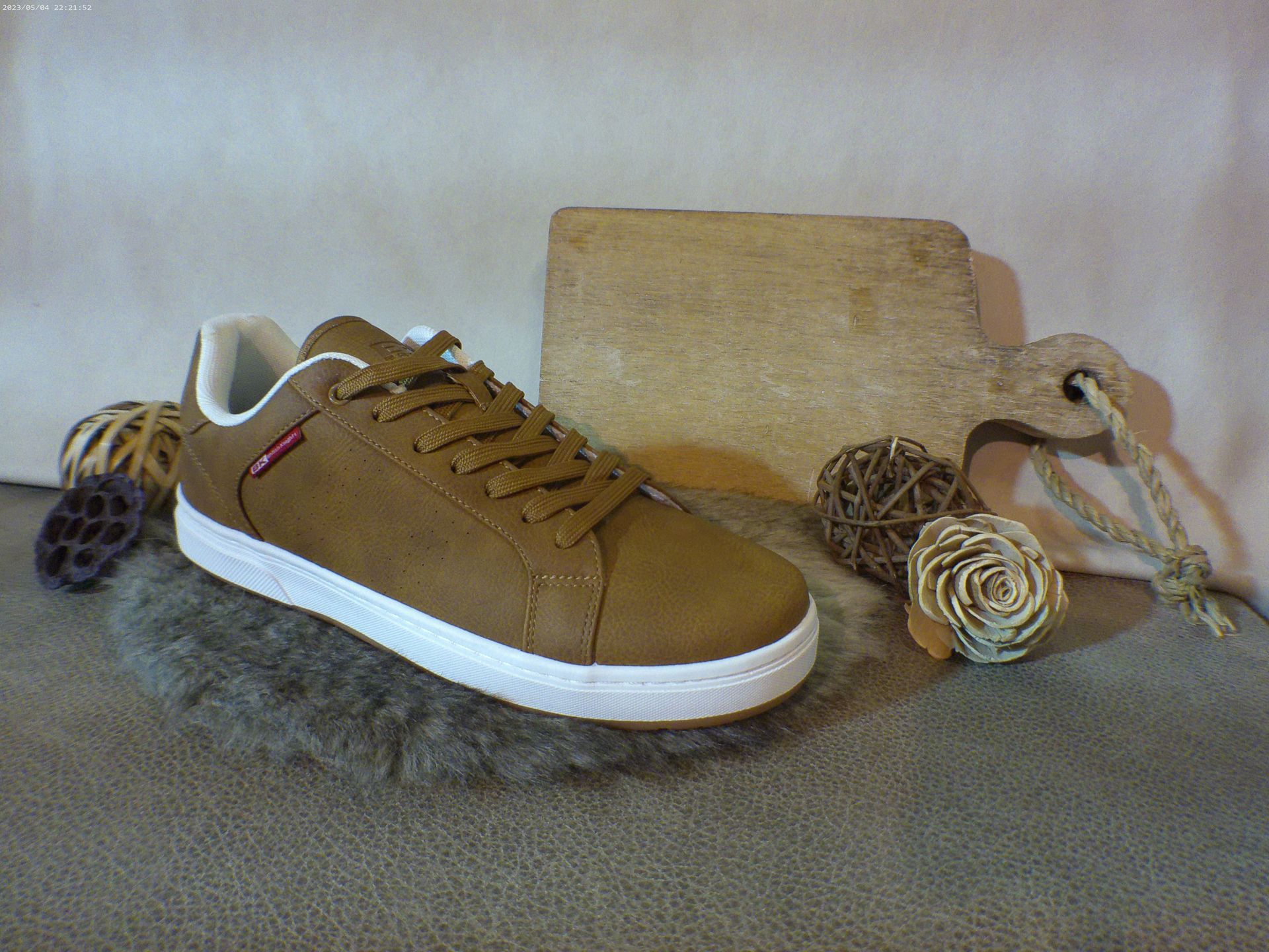 Een paar bruine sneakers liggen op een tapijt naast een houten snijplank.